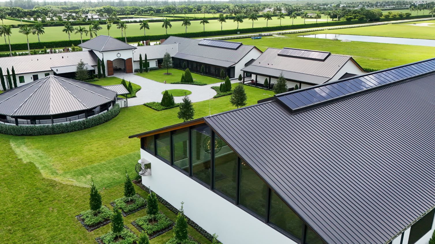 Aerial view of the 3 Graces Dressage facility featuring modern stable buildings, well-maintained gardens, and surrounding training fields