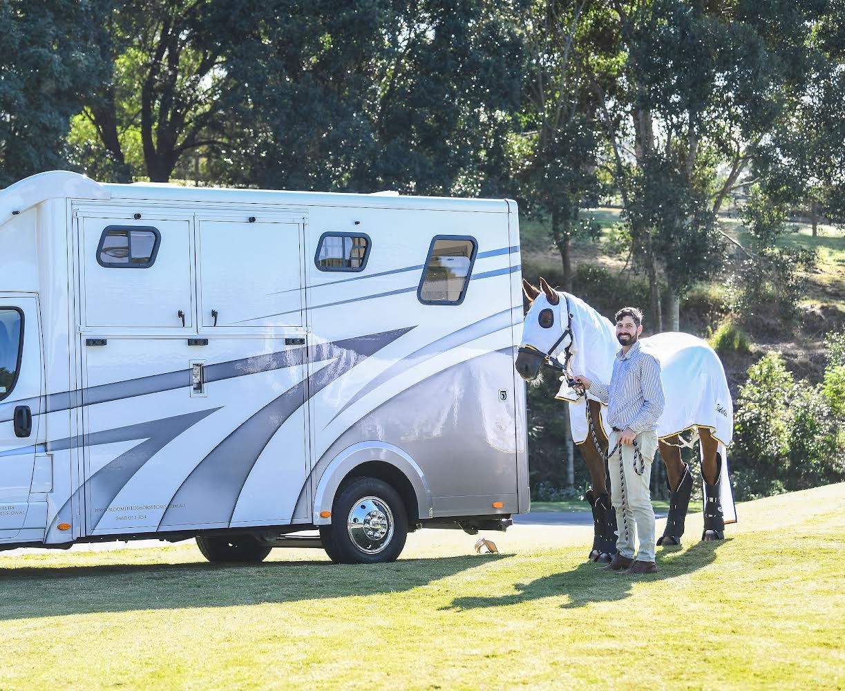 Mathew stands with his horse in front of a transporter in the Australian sun