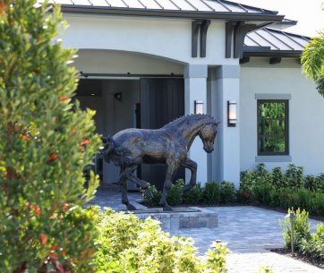 Eine bronzene Pferdestatue steht vor dem eleganten Eingang der Anlage ROasis Riding Oasis, umgeben von gepflegten Gärten.
