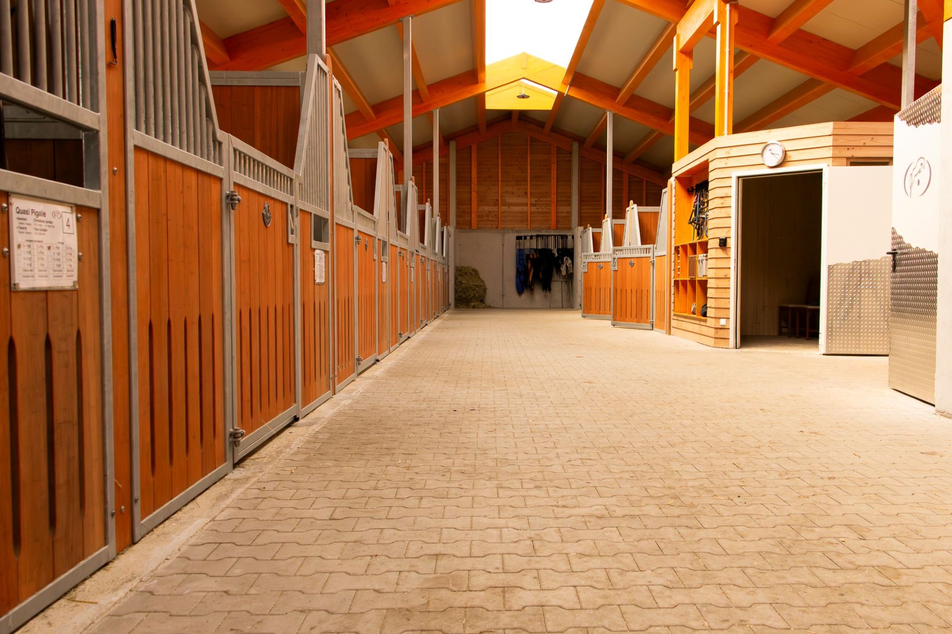 Boxes pour chevaux ouverts Pure et sellerie dans l'allée d'écurie du centre équestre Frese.