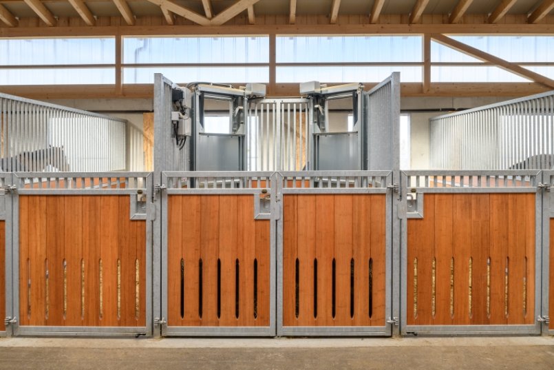 Modern hay box for automated hay feeding in a bright horse stable with metal and wood paneling.